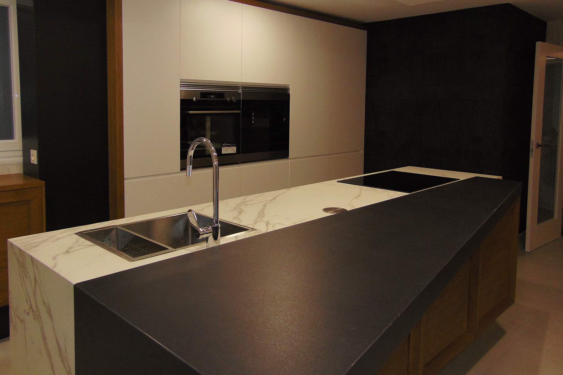 Cocina en isla con encimera en dos acabados y al fondo muebles columna