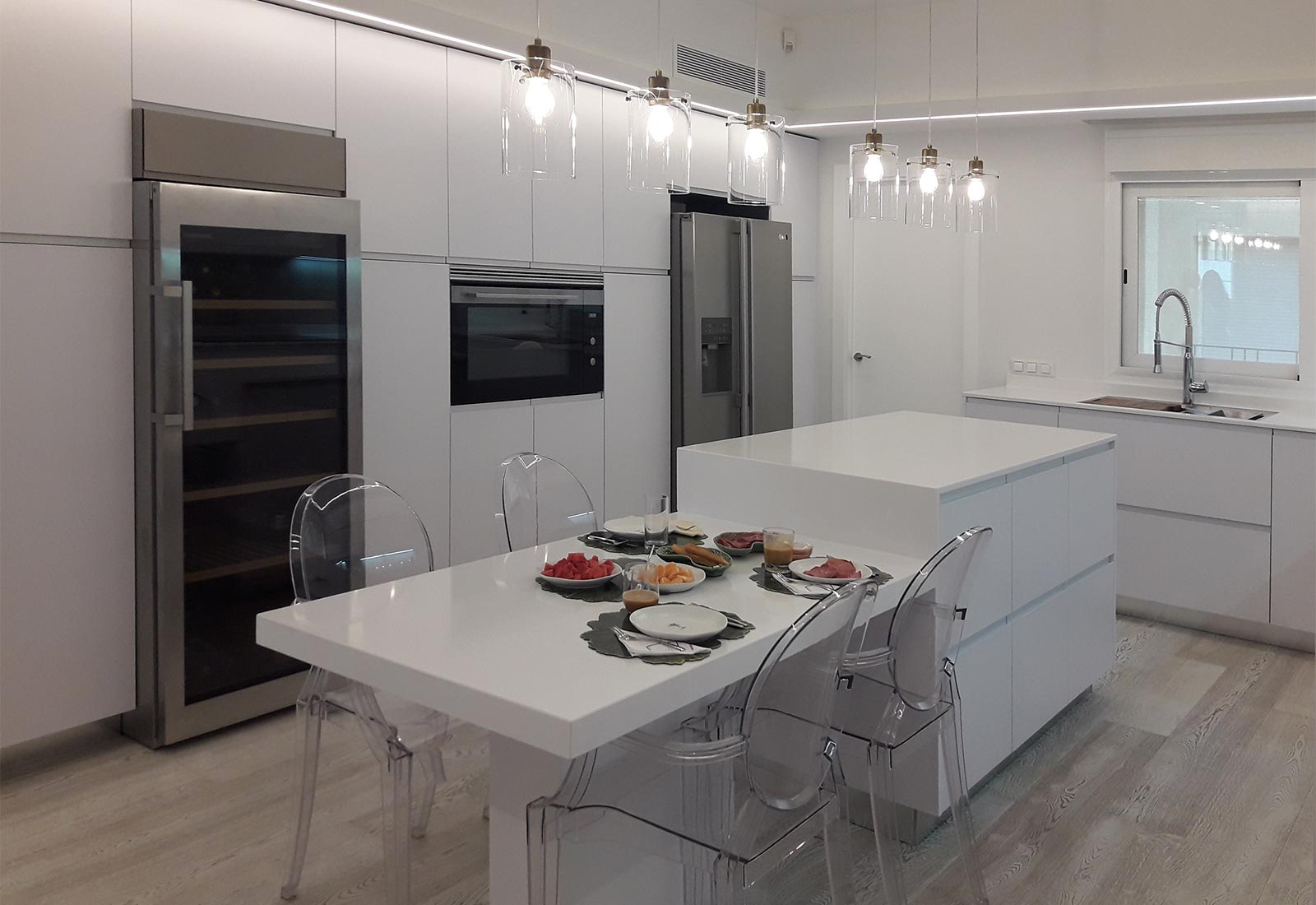 Cocina en blanco brillo con isla central y mesado, mueble columna con horno integrado, frigorífico "side by side" y vinoteca