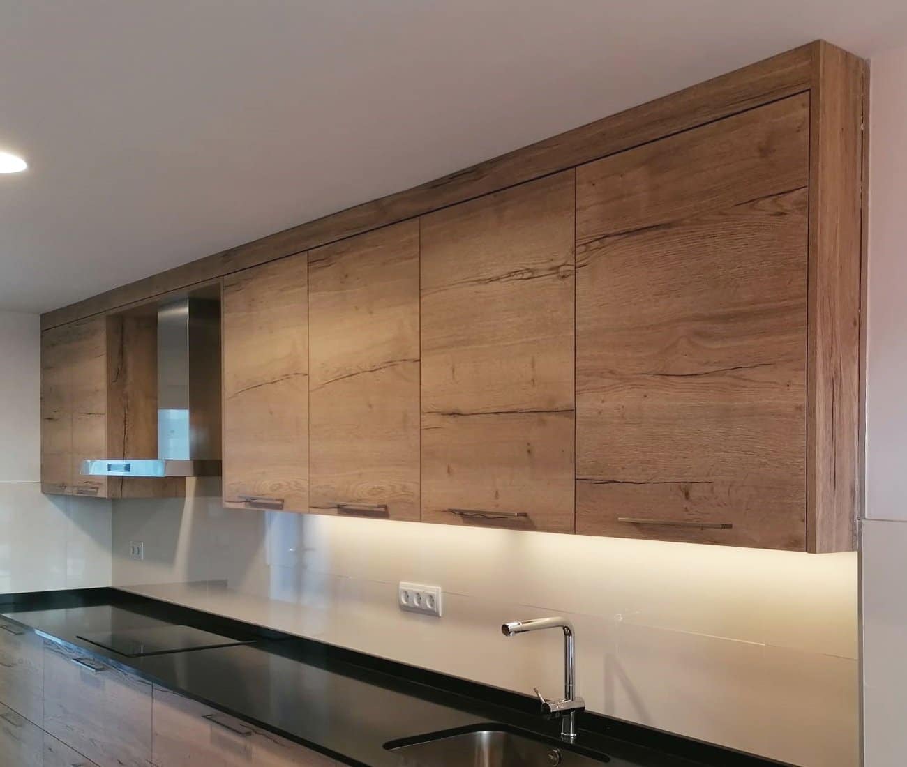 Detalle de muebles altos con LED inferios en una cocina clasica en madera con tirador