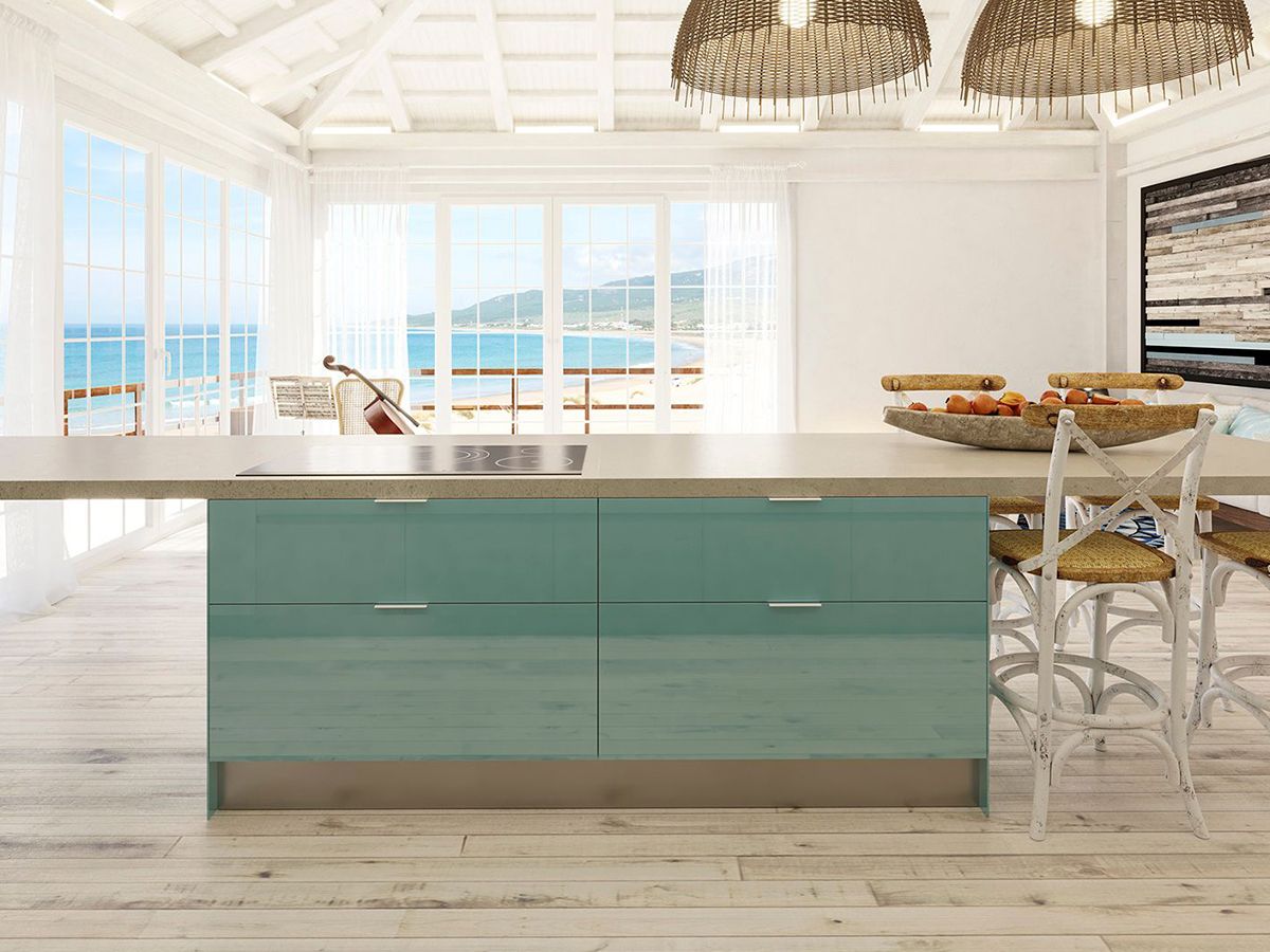 Isla de cocina lacada en azul turquesa, ubicada en una casa de playa con suelo de madera, con la playa al fondo en un día soleado