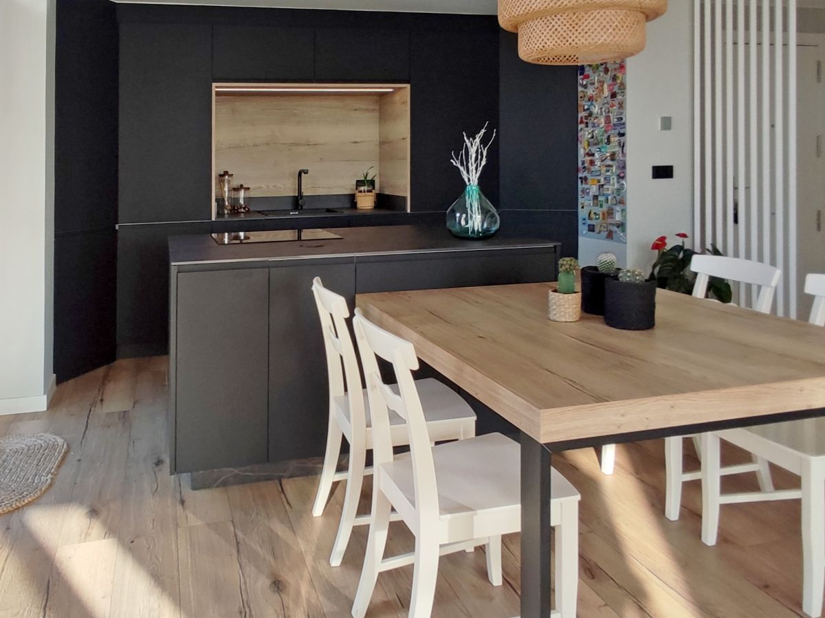 Cocina negra con detalles en madera abierta al salón con isla  y mesa integrada a esta