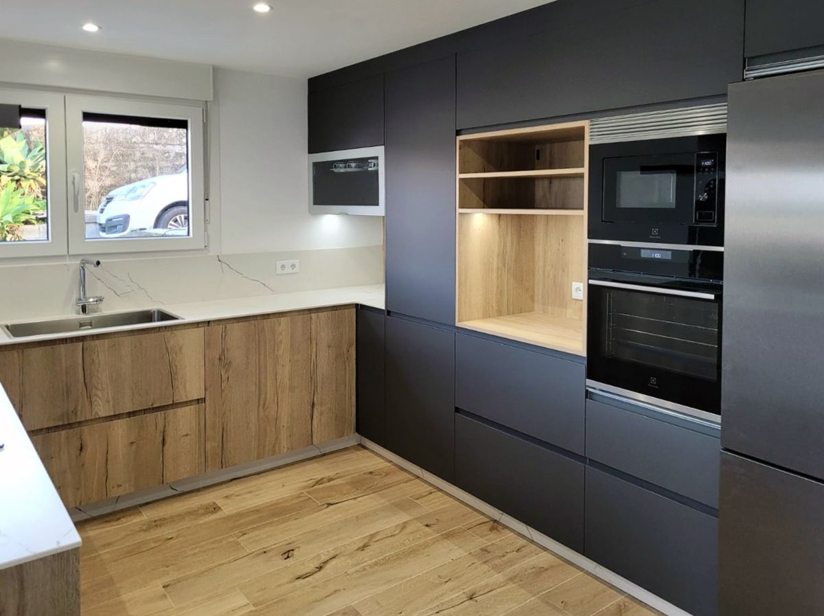 Vista lateral de cocina amplia en tonos cálidos con frente de muebles oscuros, encimera porcelánica blanca y muebles bajos en acabado madera