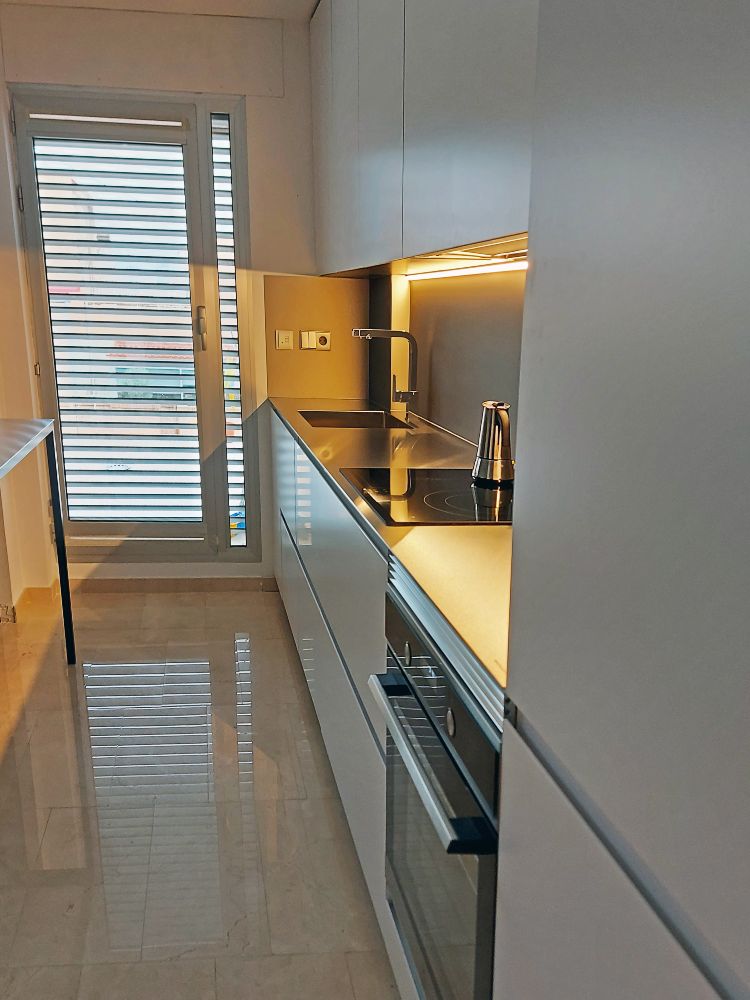 Vista lateral de cocina pequeña blanca con encimera de acero inoxidable macizo con fregadero y vitrocerámica y horno integrado en los muebles bajos