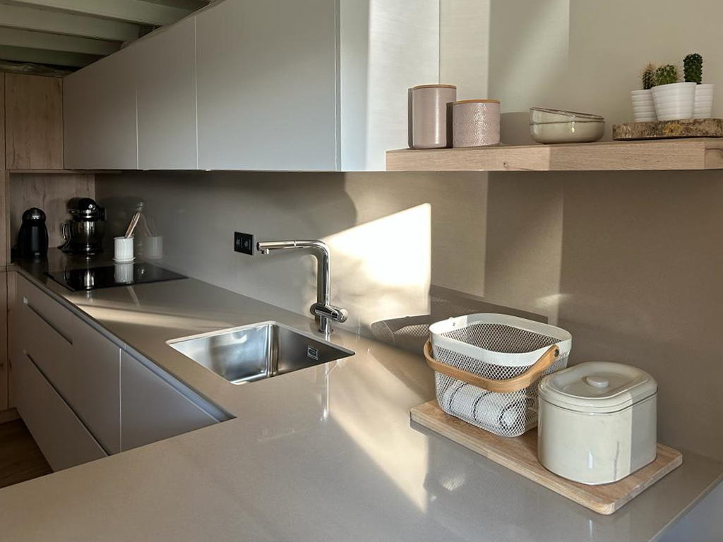 Vista en detalle de encimera gris en cocina con mobiliario blanco con fregadero y vitrocerámica integrados y botes para almacenamiento sobre estantería