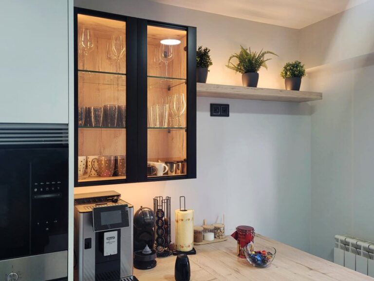 Cocina moderna en blanco y negro con mueble vitrina con puertas negras y estantes de vidrio con tazas y copas organizadas en su interior