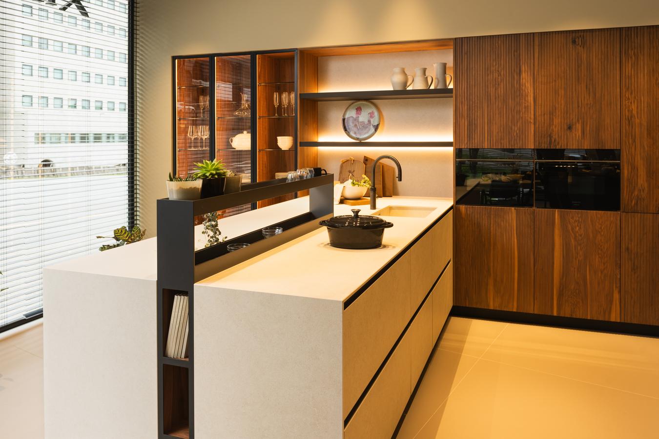 Cocina moderna en exposición Kitchen in Santiago, con península en cerámica Ananda, tres columnas vitrinas a la izquierda y mobiliario en madera natural a la derecha.