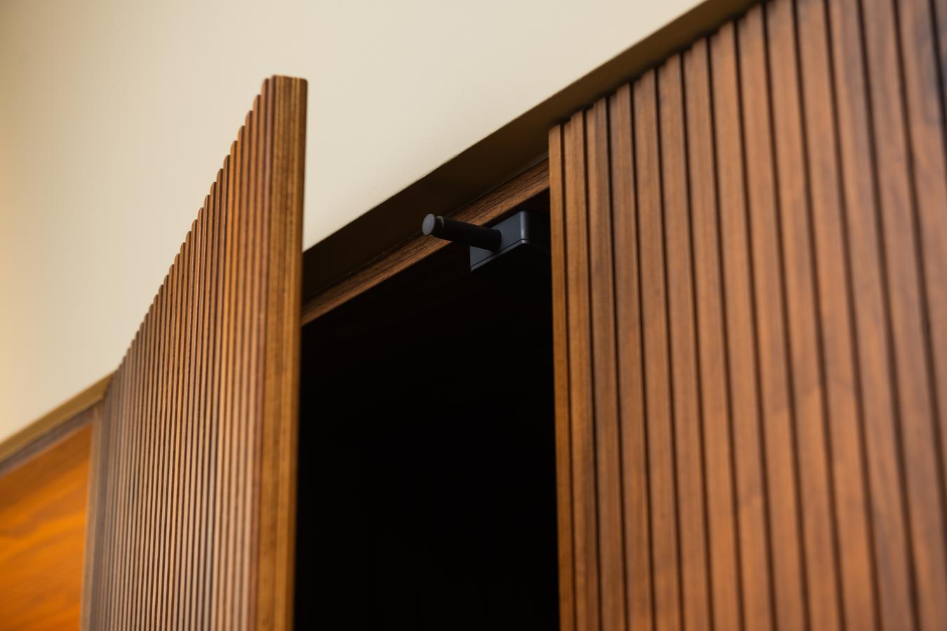 Detalle del sistema push electrónico en una puerta modelo Coral de madera natural Nogal, sin tirador, en la cocina de la exposición de Kitchen in Santiago.