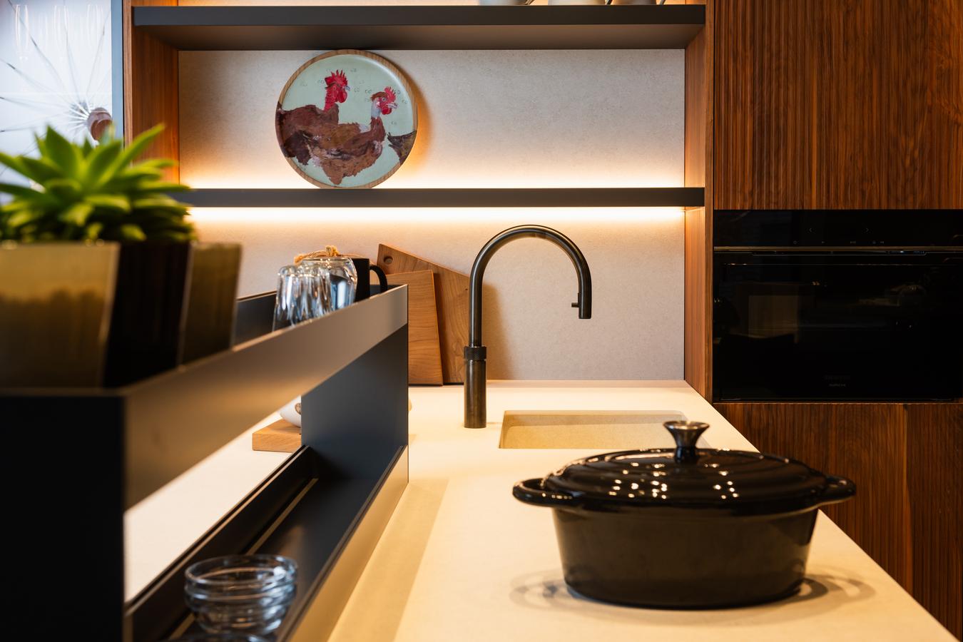 Cocina moderna de la exposición de Kitchen in Santiago, con encimera clara, mobiliario en madera, paneles decorativos y panel de crista en Negro Fénix.