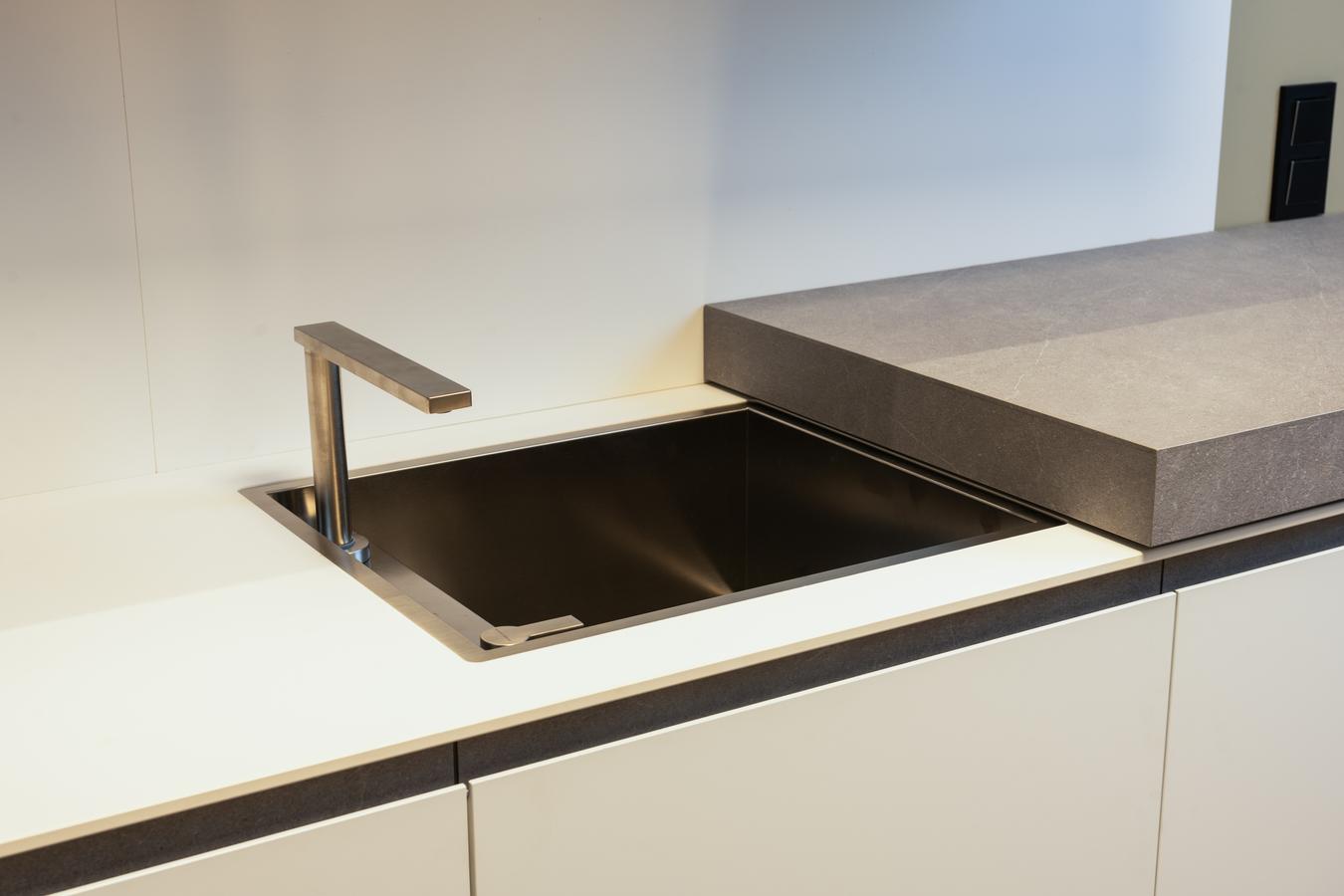 Fregadero integrado con grifo escamoteable, oculto bajo una encimera deslizante de compacto en Blanco Fénix en exposición de la tienda Kitchen in Santiago.