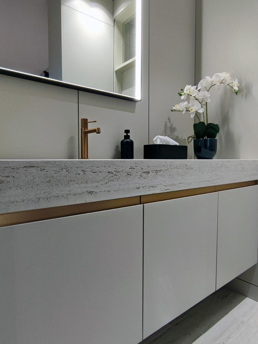 Detalle del mobiliario Fussion de Senssia en un baño moderno, con tiradores personalizados en cobre, grifería a juego y encimera con lavabo integrado en Dekton marmóreo.