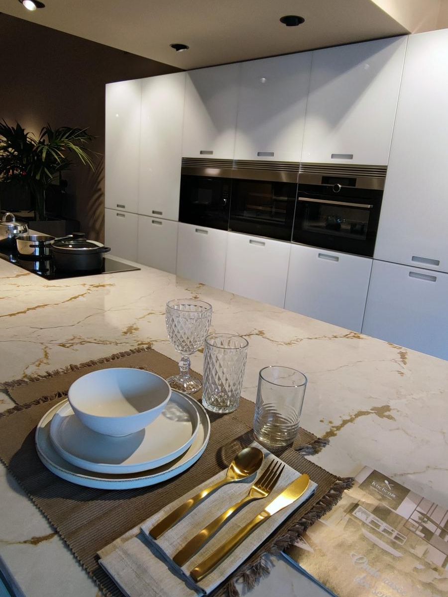 Detalle de la cocina modelo Aral de Senssia con isla suspendida en vidrio lacado blanco mate, bancada en Silestone Ivory Versailles y columnas equipadas con electrodomésticos integrados.