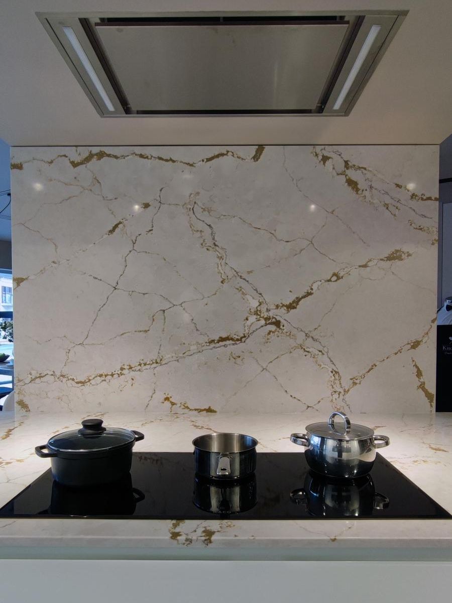 Detalle de la zona de cocción en la cocina modelo Aral de Senssia con placa de inducción integrada, bancada y forro de pared en Silestone Ivory Versailles y campana extractora empotrada.