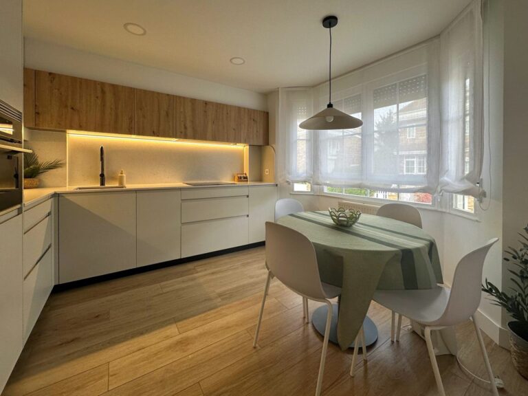 Cocina con iluminación indirecta bajo los muebles altos de Roble Dorado y mesa redonda junto a la ventana