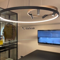 Zona de atención al cliente en la tienda de mobiliario de cocina Kitchen in Salamanca, Zona de atención al cliente en la tienda de mobiliario de cocina Kitchen in Salamanca, con gran lámpara circular, televisor para presentaciones y armario vestidor a un lado realizado íntegramente en aluminio y cristal transparente