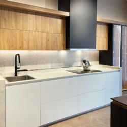 Cocina moderna con vitrina negra en Kitchen in Salamanca Interior de la moderna cocina en Kitchen in Salamanca, con muebles bajos en blanco, altos en madera con iluminación, y vitrina negra mate con cristal al fondo.