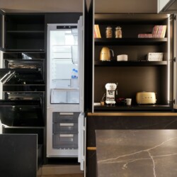 Composición de muebles columna con modelo FUSSION de Senssia en Kitchen in Salamanca Composición de mobiliario columna en aluminio y acabado cerámica con puertas abiertas con pequeños electrodomésticos en su interior y nevera y hornos abiertos