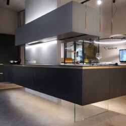Cocina en isla de diseño moderno en Kitchen in Salamanca Cocina de diseño en isla con muebles en acabados cerámica y gris, con zona de atención al cliente con TV al fondo a la derecha, y composición de muebles columna al fondo a la izquierda