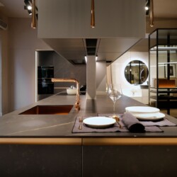 Encimera de cocina en isla de diseño moderno, con muebles altos suspendidos Vista frontal de encimera de cocina en isla de diseño moderno en color negro con detalles dorados y grifo dorado con muebles altos suspendidos