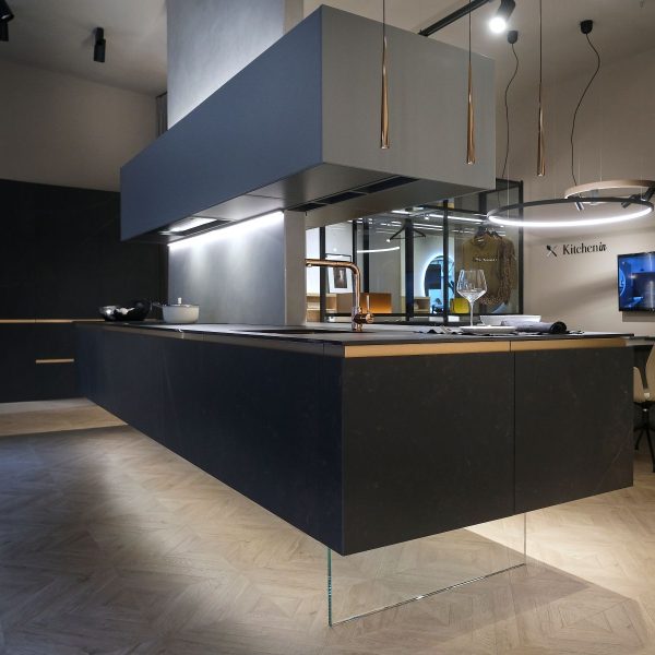 Cocina de diseño en isla en acabados cerámica y gris, con zona de atención al cliente con TV y composición de muebles columna negros