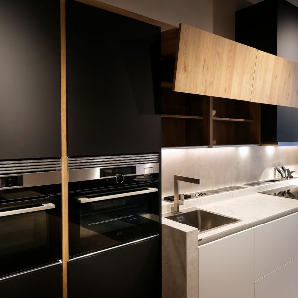 Cocina con muebles columna negros con electrodomésticos, frente de muebles bajos y altos combinados en blanco y madera y muebles columna vitrina