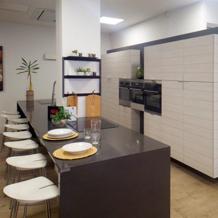 Composición de cocina en blanco y negro con electrodomésticos integrados e isla negra con vitrocerámica y fregadero