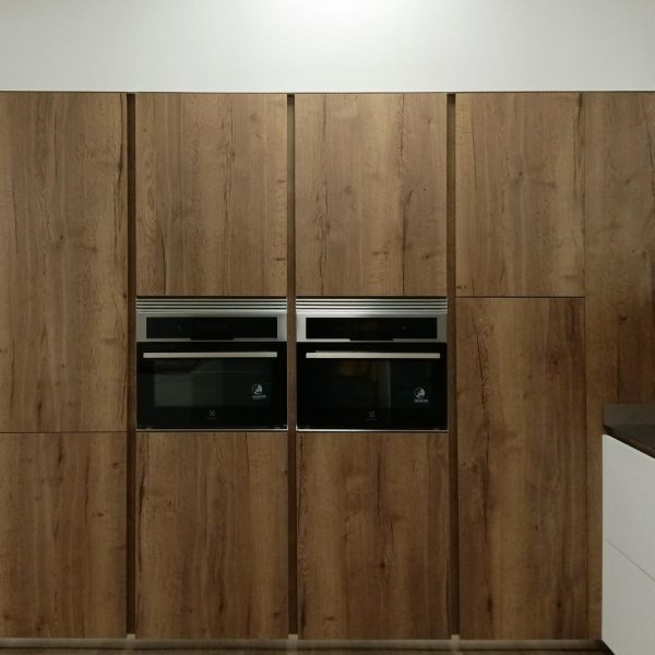 Vista frontal de mobiliario de cocina en columna en acabado madera oscuro con dos hornos integrados en el centro