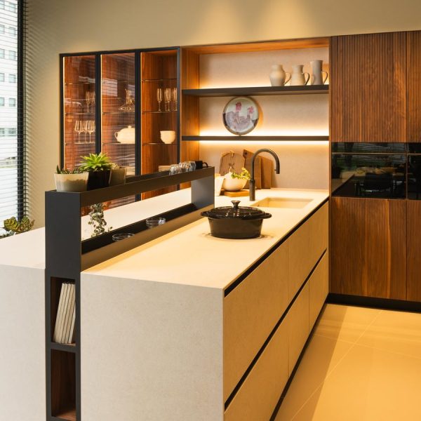 Cocina moderna en exposición Kitchen in Santiago, con península en cerámica Ananda, tres columnas vitrinas a la izquierda y mobiliario en madera natural a la derecha.