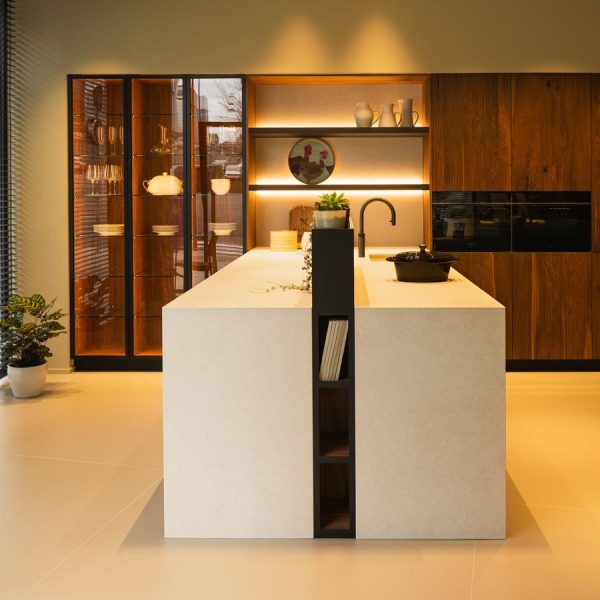 Vista frontal de cocina moderna con península en cerámica, tres columnas vitrina a la izquierda y mobiliario en madera natural a la derecha con hornos integrados