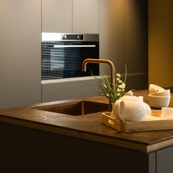 Cocina moderna con isla centrada en exposición de tienda Kitchen in con encimera Inalco UMBRA, fregadero integrado con grifo en cobre y vitro.
