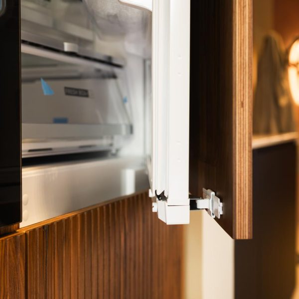 Vista en detalle de la columna frigorífico modelo Coral en madera natural Nogal, con bisagras integradas y sistema sin tiradores, en exposición Kitchen in Santiago