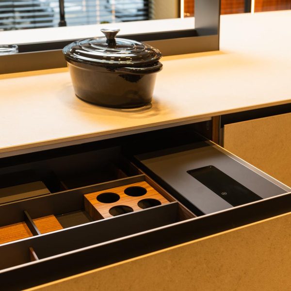 Detalle del cajón bajo placa modelo Fussion en cerámica Ananda de cocina en exposición, con compartimentos personalizados en madera y cristal.