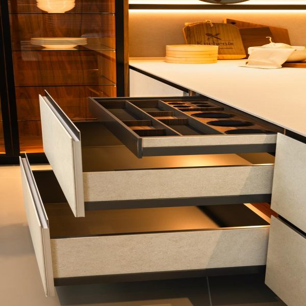 Península de cocina en exposición con mueble con cajones interiores abierto con frentes en cerámica, divisores interiores personalizados y diseño sin tiradores.