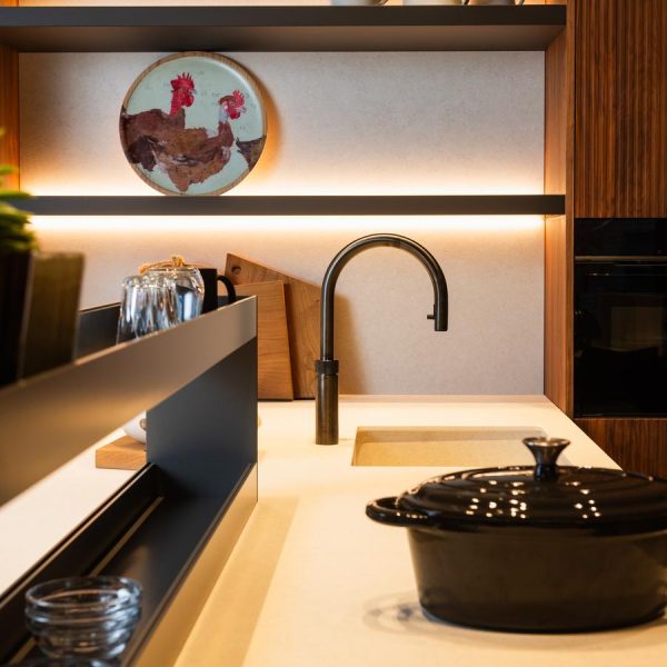 Cocina moderna de la exposición de Kitchen in Santiago, con encimera clara, mobiliario en madera, paneles decorativos y panel de crista en Negro Fénix.