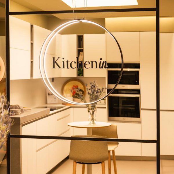 Interior tienda Kitchen in Santiago con exposición de cocina blanca en "L" y logo Kitchen in en primer plano con aro de luz alrededor