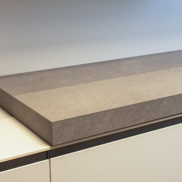 Detalle de encimera deslizante en Quartzite, con acabado en melamina color madera y base en Blanco Fénix en exposición de cocina de la tienda Kitchen in Santiago