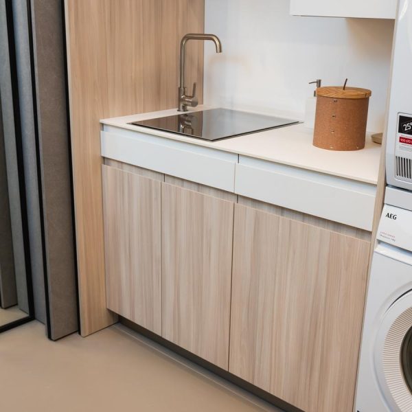 Lavandería moderna en exposición tienda Kitchen in Santiago en acabados Maple Gentle y Blanco Fénix con fregadero integrado y electrodomésticos AEG.