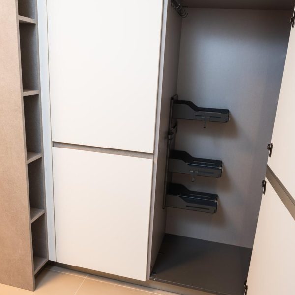 Columna escobero XL con accesorios de organización interior, puertas en Blanco Fénix y tiradores integrados, en exposición de la tienda Kitchen in Santiago.