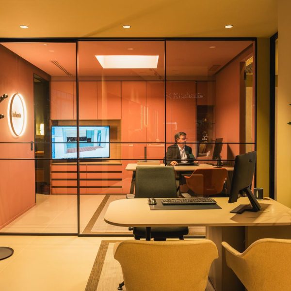 Espacio de diseño del interior de la tienda Kitchen in Santiago con decoración moderna en tonos cálidos, armarios, una pantalla con visualización 3D y mesas de trabajo con sillas