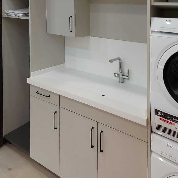 Vista lateral de composición de lavandería con mobiliario de cocina en tono beige con lavadora, secadora y fregadero